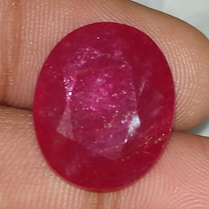 May include: A deep red oval-shaped gemstone with a faceted cut. The gemstone has a slightly sparkly appearance.