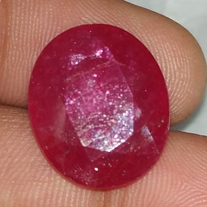 May include: A deep red oval-shaped gemstone with a faceted cut. The gemstone has a slight sparkle.