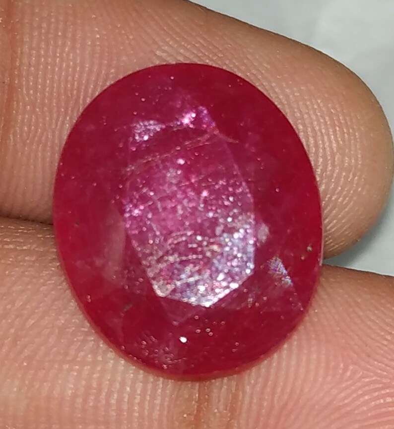 May include: A deep red oval-shaped gemstone with a faceted cut. The gemstone has a slight sparkle.