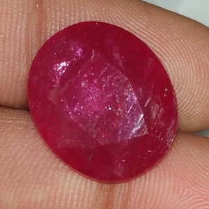 May include: A deep red oval-shaped gemstone with a smooth, polished surface.