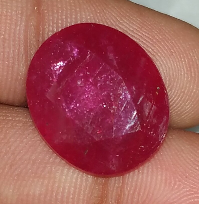 May include: A deep red oval-shaped gemstone with a smooth, polished surface.