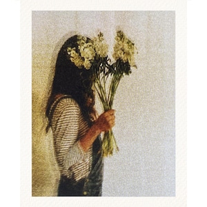 May include: A person holding a bouquet of white flowers. The person is wearing a striped top and dungarees. The background is a light-coloured wall.