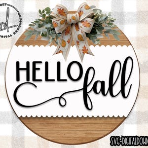 May include: A round wooden sign with a white scalloped edge and the text "HELLO fall" in black script. A fall-themed bow with orange and brown leaves is at the top of the sign.