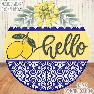 Puede incluir: Un letrero redondo de madera con un tema de limón. El letrero presenta un fondo amarillo con la palabra "hello" en escritura verde oscuro. Tiene un borde con estampado azul y blanco y está decorado con acentos de limón y hojas.