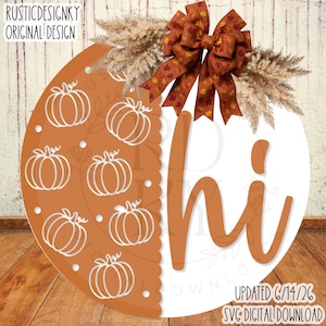 May include: A round wooden door sign featuring a split design with a burnt orange side decorated with white pumpkin outlines and a white side with the word hi in orange script. It is topped with a brown maple leaf bow and pampas grass.
