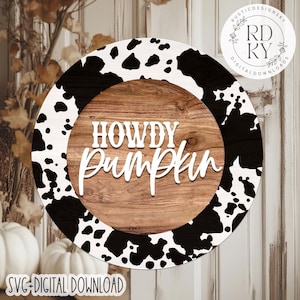 May include: A round wooden sign with a cow print border and a wood grain center. The sign reads "HOWDY Pumpkin" in white script. The bottom of the sign says "SVG DIGITAL DOWNLOAD".