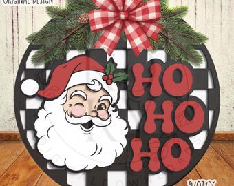 Pode incluir: Uma placa redonda de madeira com padrão xadrez preto e branco, uma ilustração do Pai Natal a piscar o olho e o texto vermelho HO HO HO. A placa é decorada com um laço xadrez vermelho e branco e ramos de pinheiro com uma pinha.