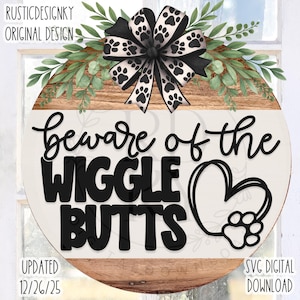 May include: Round wooden sign with the text "Beware of the Wiggle Butts" in black. The sign features a black and white paw print bow, greenery, and a heart with a paw print. The sign is a digital download.