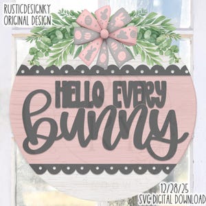 May include: A round wooden sign with the text "HELLO EVERY BUNNY" in grey script. The sign has a pink background and a grey scalloped border. It is decorated with a bow and greenery, perfect for Easter.