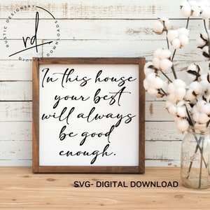 May include: A white sign with a brown frame on a wooden surface. The sign has black text that reads "In this house your best will always be good enough."
