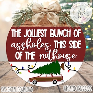 Puede incluir: Un adorno navideño redondo con el texto "THE JOLIEST BUNCH OF assholes THIS SIDE OF THE nuthouse." El adorno presenta un coche marrón con un árbol de Navidad encima, luces de cadena y un lazo. También se ven las palabras "SVG DIGITAL DOWNLOAD" y "UPDATED 08/29/25".