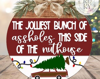 May include: A circular Christmas decoration with the text "THE JOLIEST BUNCH OF assholes THIS SIDE OF THE nuthouse." It features a brown car carrying a Christmas tree, string lights, and a bow. The words "SVG DIGITAL DOWNLOAD" and "UPDATED 08/29/25" are also visible.