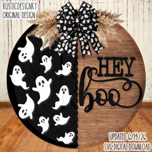 May include: A round wooden door sign featuring a split design. The left side is black with white ghost illustrations. The right side has a natural wood grain finish with the black text HEY BOO. A black and white ghost patterned bow sits on top.