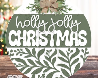 Pode incluir: Um enfeite de Natal redondo com as palavras "holly jolly CHRISTMAS" em branco. O enfeite tem um fundo verde e um design floral decorativo na parte inferior. É encimado por um laço de serapilheira e folhagem.