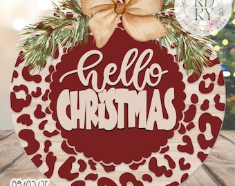 May include: Circular Christmas sign with a red and cream leopard print design. The sign features the words "hello CHRISTMAS" in a layered, cursive font. A cream-coloured bow and pine branches adorn the top. The sign is a digital download.