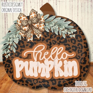 May include: A pumpkin-shaped wall sign with a brown leopard print pattern, featuring the text 'hello pumpkin' in white and orange. The design includes a decorative bow with a pumpkin and leopard print, and green leafy sprigs.