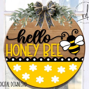 May include: A round wooden sign with the text "hello honey bee" in black and yellow lettering. The sign has a black and white polka dot border and a yellow background with white flower designs. A cartoon bee with black and yellow stripes is on the right side of the sign.