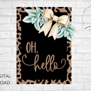 May include: A black and brown leopard print background with a black square frame. Inside the frame is a gold bow with green leaves and the text "OH. hello" in brown script.