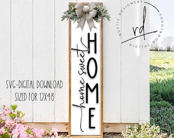 May include: A wooden sign with a white background and black lettering that reads "home sweet home". The sign is decorated with a green wreath and a white bow.