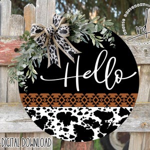 May include: Black and white cowhide patterned round door hanger with a brown geometric border and the word "Hello" in white lettering.