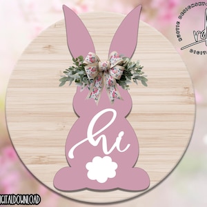 May include: A pink bunny rabbit silhouette with a floral wreath and a bow. The bunny is holding a white "hi" sign. The background is a light wood grain.