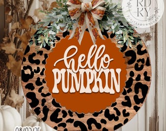 May include: Circular wooden sign featuring a leopard print design and an orange pumpkin-shaped centre. The sign reads "hello PUMPKIN" in white script. It is adorned with a bow and foliage. The sign is a digital download.