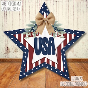May include: A patriotic star-shaped decoration with a white inner star and the word "USA" in navy blue. The star features red and white stripes, navy polka dots, and a burlap bow. The design includes greenery accents.