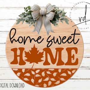 May include: A round wooden sign with the text "home sweet HOME" in black and orange lettering. The sign is decorated with a brown and white bow and a wreath of green leaves. The background is a white woodgrain pattern.