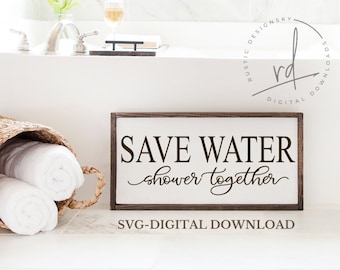 Puede incluir: Un letrero de madera marrón con texto blanco que dice "Save Water shower together" y "SVG-DIGITAL DOWNLOAD". El letrero está en un baño con una bañera blanca y toallas en una cesta.