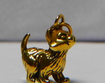 May include: A gold-colored charm in the shape of a small puppy. The charm has a loop at the top for attaching to a necklace or bracelet.