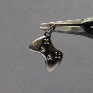 Puede incluir: Un charm de plata con forma de mando de videojuego. El charm tiene un pequeño bucle en la parte superior para sujetarlo a un collar o pulsera.
