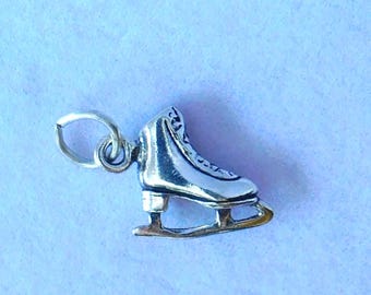 Peut inclure: Un charm en forme de patin à glace argenté, avec des détails de lacets et de lame. Le charm est conçu avec une boucle pour l'attache. Le fond est bleu clair.