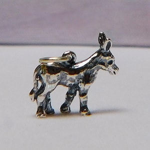 May include: A small, silver-colored donkey charm with a detailed design. The charm features a loop for attaching to a necklace or bracelet. The donkey is depicted in a standing position, with its ears perked up and its tail down.