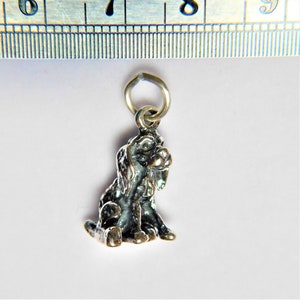 May include: Silver charm of a small, sitting dog. The dog is detailed with a textured fur pattern and has a small, round nose.