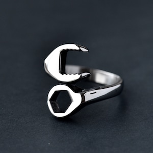 May include: A silver ring shaped like a wrench. The ring has a hexagonal opening and a curved handle.