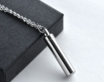 May include: A silver chain necklace with a cylindrical pendant. The pendant is made of metal and has a smooth, polished finish.