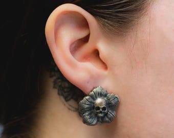 May include: A pair of silver earrings shaped like flowers with a skull in the center of each flower.