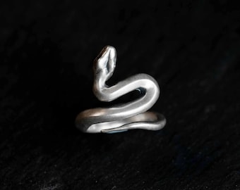 May include: A silver-toned snake ring. The ring is coiled, with the snake's head raised. The ring appears to be made of metal and has a polished finish. The snake's head is detailed with eyes and a slightly open mouth.