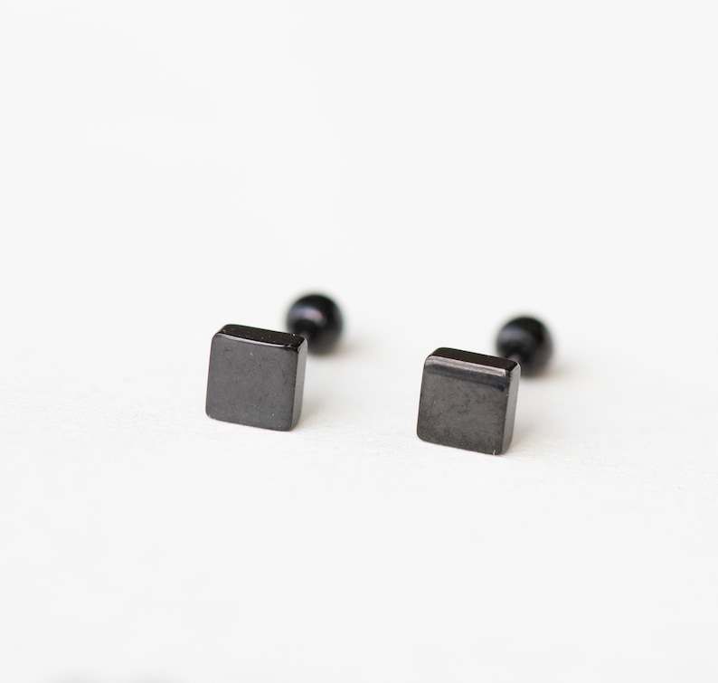 May include: A pair of black square stud earrings with a small ball on the back.