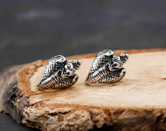 May include: A pair of silver-colored snake-shaped stud earrings. The earrings are detailed with scales and a serpent head. The earrings are displayed on a wooden surface with a dark background.