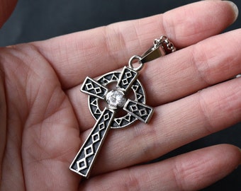 May include: Silver Celtic cross pendant with a clear rhinestone in the center. The cross has a black enamel design.