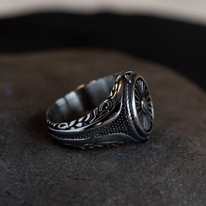 May include: A silver ring with an intricate design featuring a circular pattern and floral details. The ring is made of metal and has a polished finish.