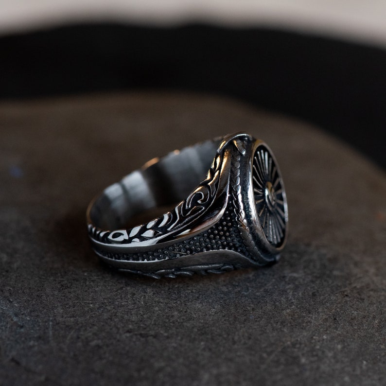 May include: A silver ring with an intricate design featuring a circular pattern and floral details. The ring is made of metal and has a polished finish.