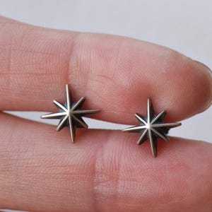 May include: A pair of silver star-shaped stud earrings. The earrings are small and delicate, with a simple design.