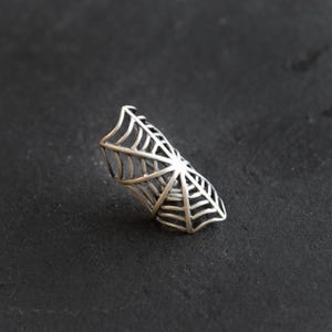 Op de afbeelding: Een zilveren spinnenweb ring. De ring is gemaakt van metaal en is gevormd als een spinnenweb. Het is een statement sieraad dat perfect zou zijn voor een Halloween feest of een gothic-geïnspireerde outfit.