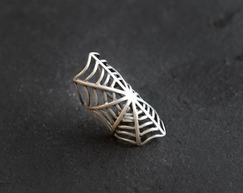 Puede incluir: Un anillo de araña de plata. El anillo está hecho de metal y tiene forma de telaraña. Es una pieza de joyería llamativa que sería perfecta para una fiesta de Halloween o un atuendo de inspiración gótica.