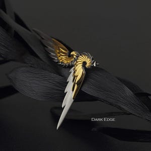 May include: A gold and silver wing-shaped earring with a detailed design. The earring is on a black background with the text "DARK EDGE".