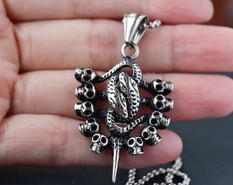 May include: A silver pendant necklace featuring a detailed design of a snake with multiple skulls surrounding it. The pendant is attached to a silver chain.