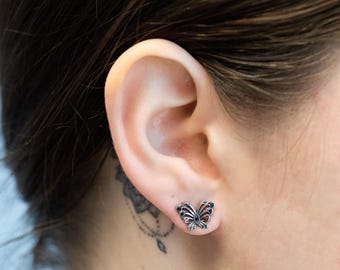 May include: A pair of silver butterfly earrings with black accents. The earrings are small and delicate, and they would make a great gift for someone who loves butterflies.
