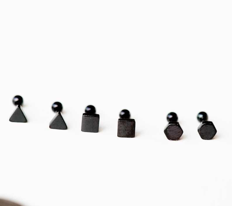 May include: Six black stud earrings with different geometric shapes: triangle, square, and hexagon. The earrings are made of metal and have a black finish.